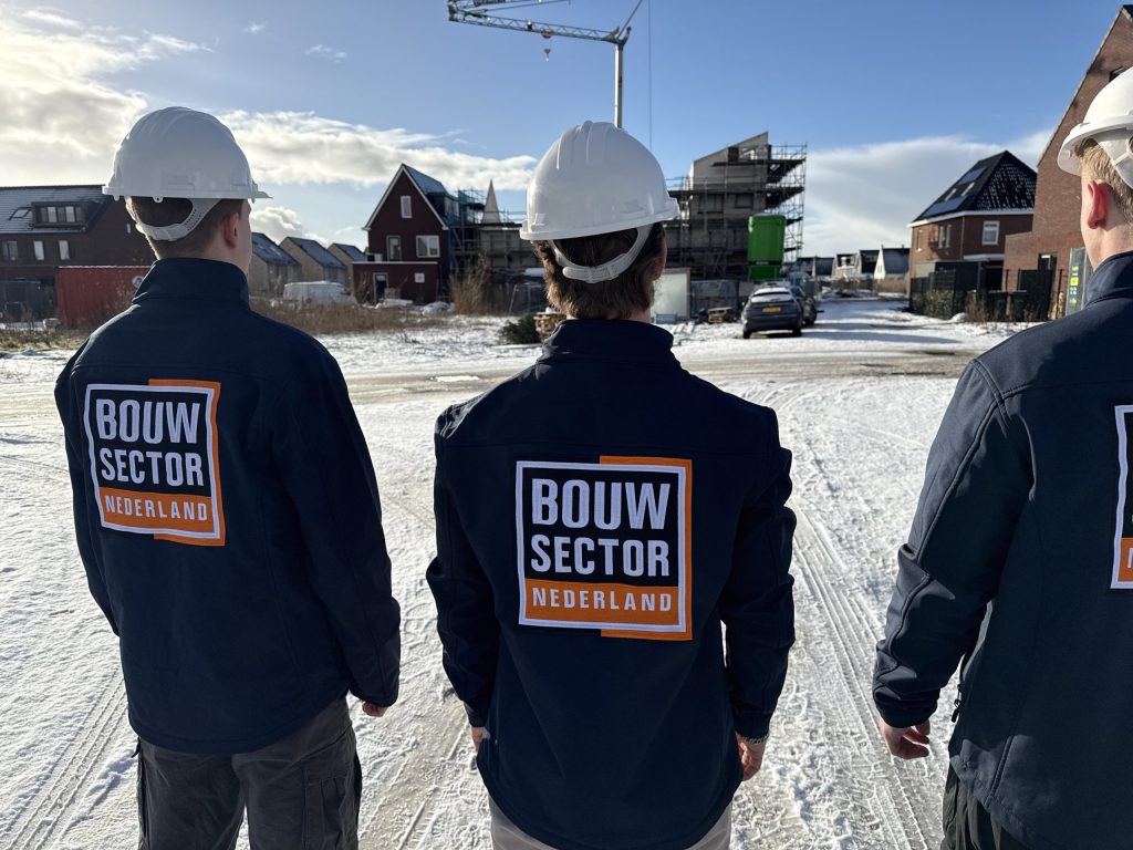 Drie vakmensen van Bouwsector Nederland met witte helm bij een rij woningen in aanbouw